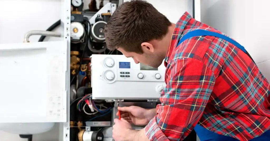 Maintenance chaudière : service de dépannage professionnel Technicien réparant une chaudière blanche avec un tournevis, révélant le panneau de contrôle et le câblage interne.